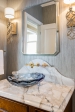 The wall is done in grey striae treatment, and sconce lighting replaced an over-mirror light. The new emerald-cut mirror and crystal bowl sink w/ marble countertop add decadence.