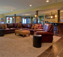 In the lower level, we did a complete gut and refinish. From the glass-enclosed workout area to the bar, red leather sectional, and even the scone lighting on the pillars, everything was new.