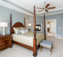 A reverse angle of the bedroom looking into the bathroom. The new soft blue ottoman at the foot of the bed and the bedding and pillows add more contrast with the brown furniture.